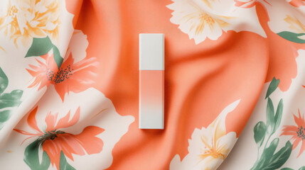 Coral-colored cosmetic product rests on a floral fabric. Soft, summery vibes.