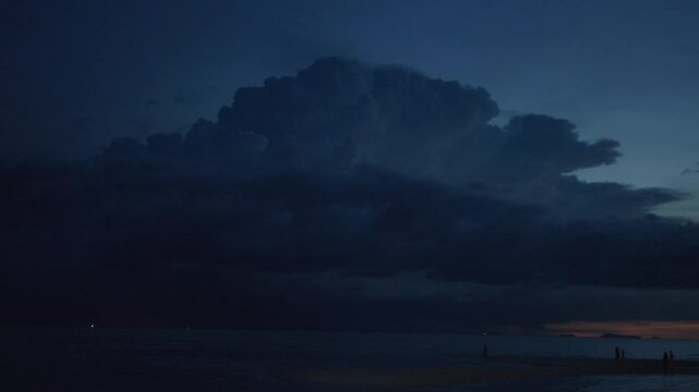 Flashes of lightning in a huge thundercloud that covers the evening sky. The moment of approach of a strong thunderstorm over the sea after sunset. The power of nature and the elements