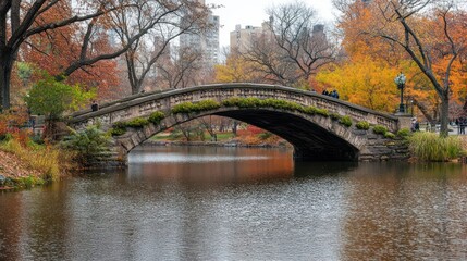 Obraz premium Stone arch bridge over calm autumnal lake in city park.