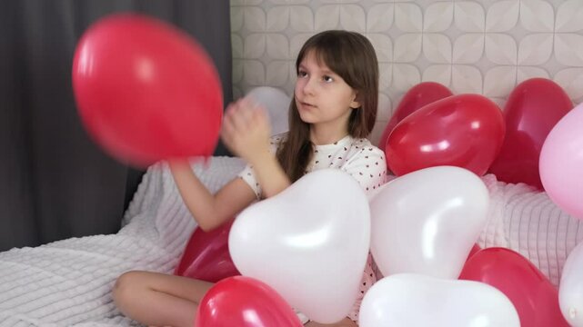 ittle girl surrounded by red balloons. in the shape of heart is having fun and fooling around. Valentine's Day concept. Blurred motion. 