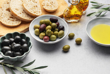 Bowls with green and black olives, olive oil and sliced bread on a wooden cutting board