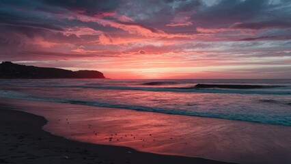 Fototapeta premium Vibrant sunset with rich pink and orange hues reflecting on calm beach waves against a darkening sky creating a serene coastal atmosphere
