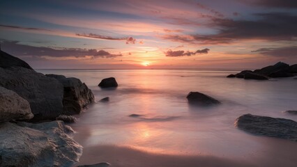 Fototapeta premium Serene sunset over tranquil waters with smooth waves reflecting orange and purple hues, rocky foreground positioned on the left, peaceful atmosphere.