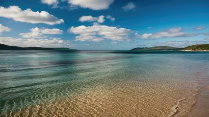 Serene coastal landscape with gentle ripples on clear water under a vibrant blue sky and fluffy white clouds near a tranquil beach setting