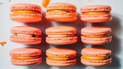 Fototapeta premium Pink macarons arranged in two rows on a clean white background, featuring a soft orange filling that creates a visually appealing dessert display.