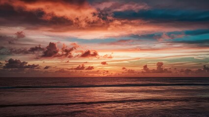 Naklejka premium Tranquil ocean horizon at sunset with vibrant orange and blue hues reflecting on calm water and dramatic cloud formations above