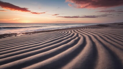 Fototapeta premium Coastal shoreline at sunset with wavy sand textures in soft beige and warm hues of orange and pink in the sky with gentle waves approaching