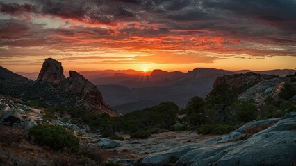 Fototapeta premium Dramatic sunset landscape with vibrant red and orange hues illuminating rocky formations and distant mountains under a moody sky 1