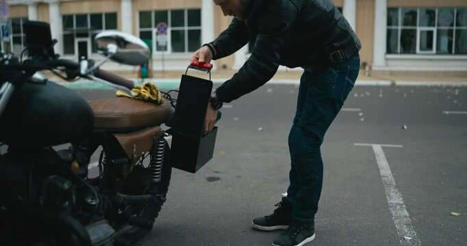 Man placing tools into the custom side compartment of a vintage motorcycle in an urban parking lot setting