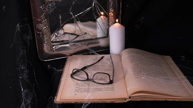 Oggetti abbandonati, libro, specchio rotto e occhiali con ragnatele, candela accesa 