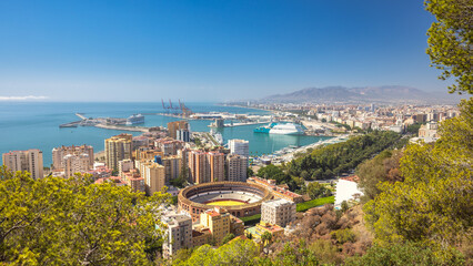 Malaga, seaside city in Andalusia, Spain, Europe. Coastal city skyline with harbor, buildings, and a bullring.  A sunny day overlooking the Mediterranean.