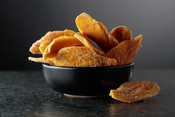 Dried mango slices in a black dish on a black background.