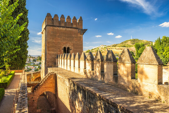 Alhambra complex in Granada town, Andalusia, Spain. Ancient fortress walls and tower overlooking a cityscape under a vibrant blue sky.