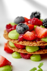 A vibrant and refreshing mille-feuille dessert, layered with fresh berries and a light cream. The dessert is garnished with a sprig of mint, creating a visually appealing and appetizing composition