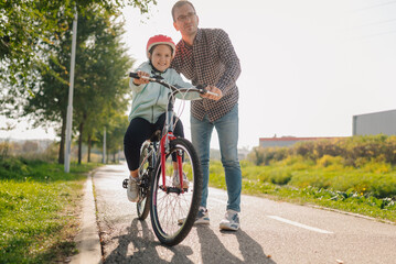 Obraz premium Father teaching daughter riding bicycle in park during sunny day