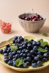 Blueberry dish with copper spoon, next to a bowl of cherries and a small jar with pomegranate seeds, decorated with mint leaves. Concept of fruit, fresh food and healthy eating