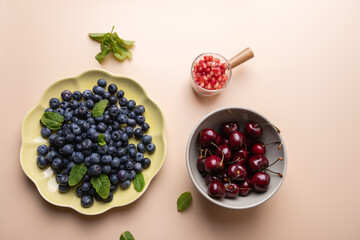 View from above of blueberries, cherries and pomegranate seeds with mint leaves on beige background. Minimalist and colorful composition of fresh fruits. Healthy eating and summer concept