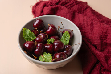 Close-up of a bowl with cherries and mint leaves, accompanied by red fabric on neutral background. Minimalist and elegant style. Concept of healthy eating and natural products