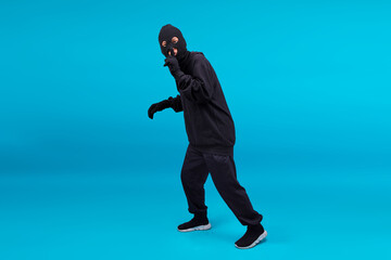 Full Body Shot Of Thief In Black Clothes Wearing Mask Gesture Silence To Front Isolated On Blue...