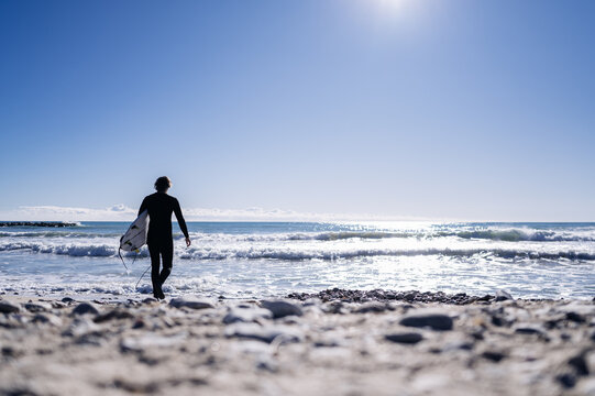 Surfer walking into ocean on sunny day with surfboard