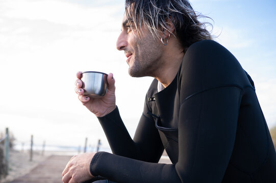 Surfer drinking hot beverage on beach boardwalk - Powered by Adobe