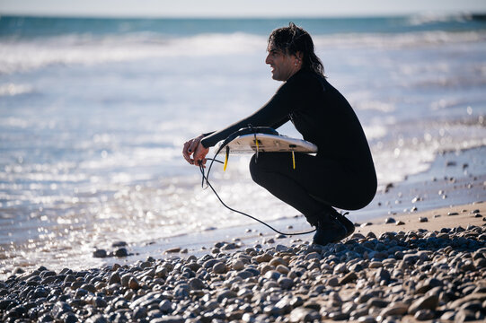 Surfer crouching on the beach holding his surfboard