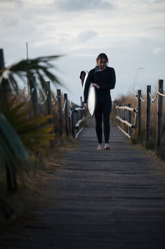 Surfer walking on wooden footbridge at sunset carrying surfboard
