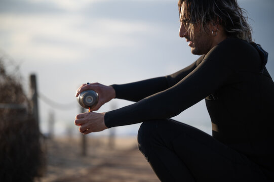 Surfer pouring hot beverage into hands on beach