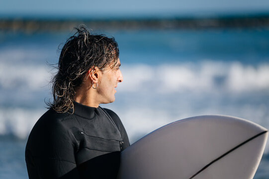 Surfer holding surfboard watching ocean waves on sunny day