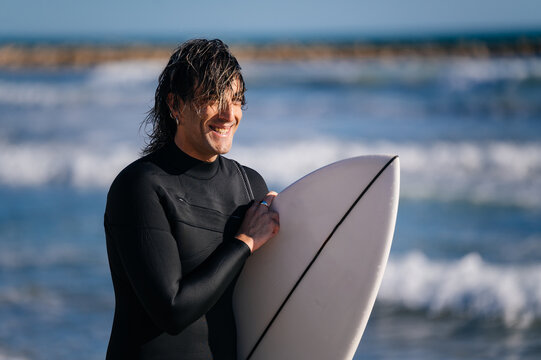Smiling surfer holding surfboard on beach, enjoying ocean waves