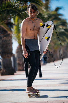 Surfer riding skateboard while carrying surfboard on tropical beach