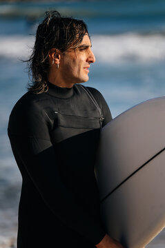 Surfer wearing wetsuit holding surfboard looking at ocean waves