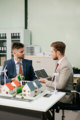 Experts collaborate on renewable energy solutions with house models, wind turbines, and solar panels,