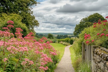 Obraz premium Garden path with pink flowers leading to a scenic view for landscaping, travel, or backgrounds