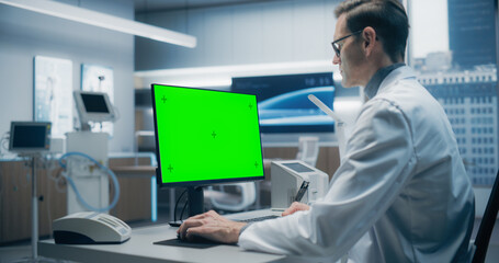 Male Scientist in a White Lab Coat Works on a Green Screen Computer in a Modern Medical Lab, Focusing on Research and Healthcare Analysis in a High-tech Hospital Environment