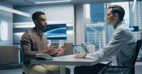 Male Specialist Discusses Health Data With a Male Patient in a High-tech Medical Lab, Utilizing...