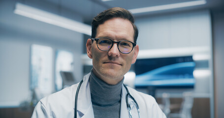 Obraz premium Confident Male Physician in a Hospital Office, Wearing Glasses and a Stethoscope, Confidently Turns and Looks at Camera. Medical Help and Healthcare Solution, Modern Healthcare