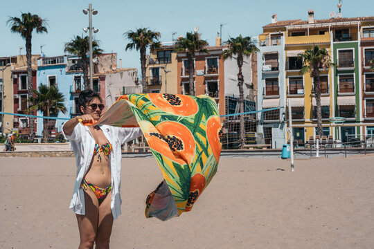 Woman spreading her beach towel on the sand on a sunny day - Powered by Adobe