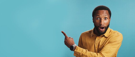 Surprise, pointing or portrait of black man by space for breaking news, announcement or sales offer. Blue background, shocked face or African person in studio with omg expression for discount mockup