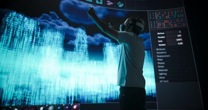 Young Male Architect Creates a Parametric Design of a Whole Futuristic City with Skyscrapers, Wearing a Virtual Reality Headset and Interacting with a Digital Polygon Mesh on a LED Screen