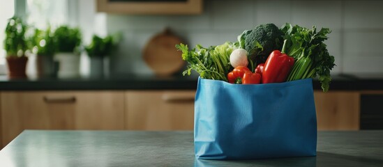 Reusable blue shopping bag filled with fresh vegetables on a kitchen counter featuring greens red bell peppers with a modern kitchen backdrop.