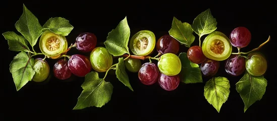 Crédence de cuisine Cuisine Freshly sliced grapes in green and purple hues arranged with lush green vine leaves on a black background create an elegant culinary display.  © Nijat