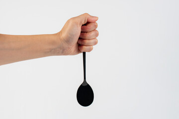 Hand and metal black spoon on white background