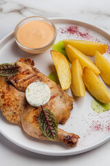Top view of a delicious grilled chicken served with potato wedges, a creamy sauce, and herbs on a white plate, creating an enticing culinary scene. Restaurant or cafe menu, cookbook recipe