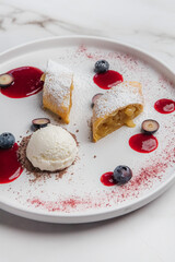 Apple strudel with powdered sugar, accompany a scoop of vanilla ice cream, drizzled with berry coulis and topped with fresh blueberries and chocolate shavings. Restaurant or cafe menu, cookbook recipe