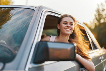 Young woman enjoying a drive with her head out of the car window, conveying joy and freedom in a...