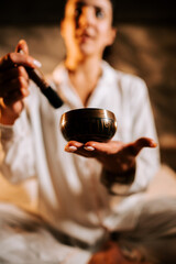 Woman participates in mindfulness session using Tibetan singing bowl for relaxation and meditation in a tranquil setting