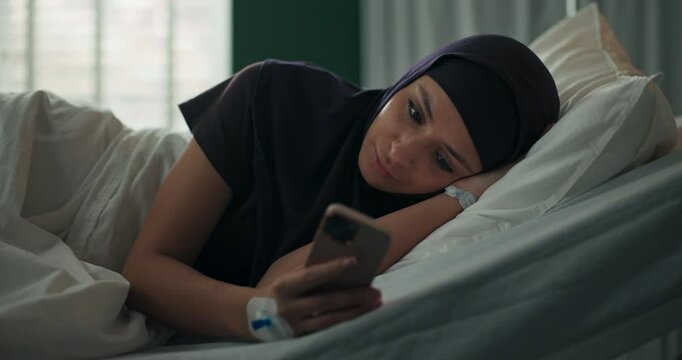 Arab patient in hospital bed, scrolling through messages on her phone, a moment of respite in her medical journey.
