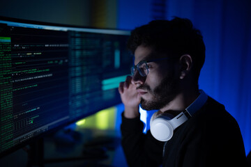 Young man focused on programming in a dim workspace, glowy screens display complex codes and data...