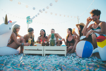 Group of friends making party on the beach at sunset time